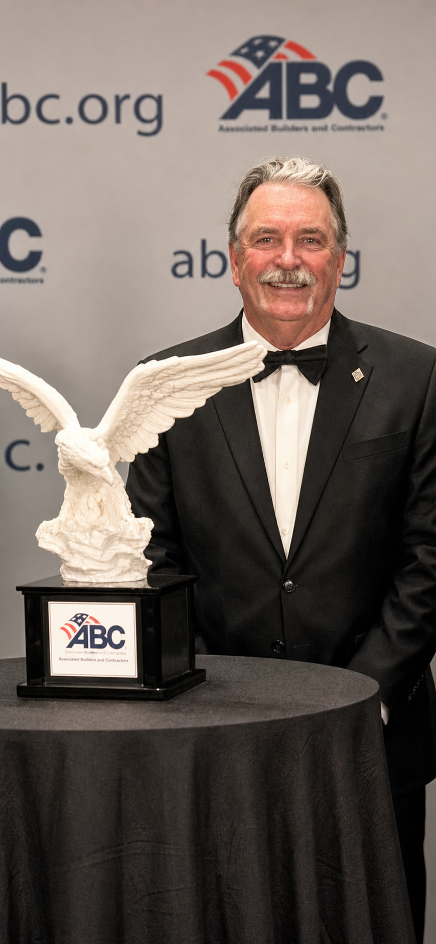 Clyde Pershall in a tuxedo and bow tie beside an eagle award